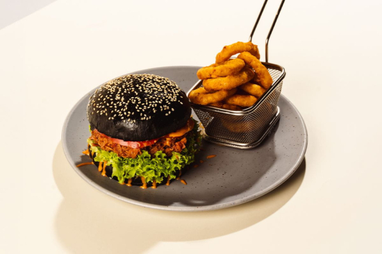 Czarny burger z szarpaną wieprzowiną, krążkami cebulowymi i sosem sriracha